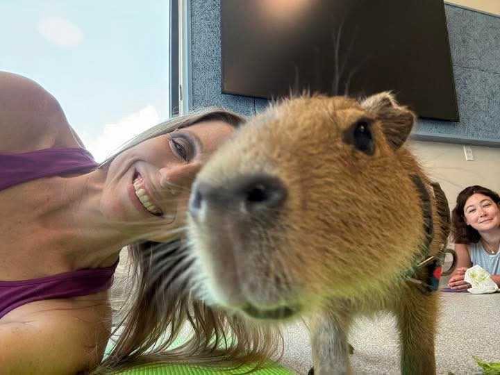 Woman posing with a Capybara at Capybara Yoga